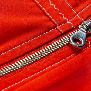 Close-up of a silver zipper running along bright red fabric with white stitches showing the seam.