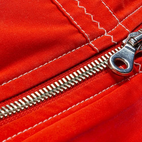 Close-up of a silver zipper running along bright red fabric with white stitches showing the seam.