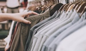 Person's hand browsing a row of brown and gray shirts on hangers in a clothing store rack