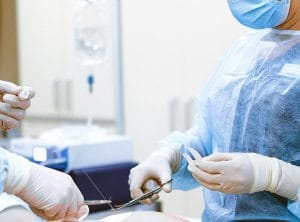 Surgeons in scrubs and masks perform a surgical procedure, handling sutures and instruments in a sterile setting.