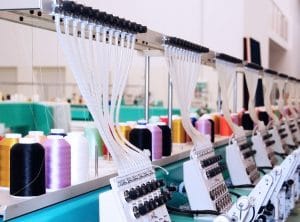 Industrial embroidery machine with multiple thread spools feeding into sewing heads in a textile factory setting