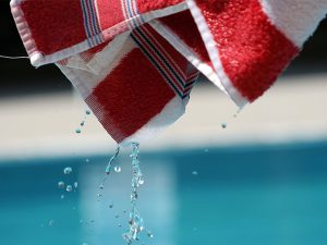 Red and white striped towel dripping water above a swimming pool surface