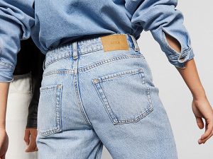 Back view of a person wearing light-wash jeans with a brown leather patch on the waistband and a blue denim shirt.