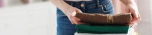 Person folding a brown towel atop a stack of green and white towels in a bright laundry space