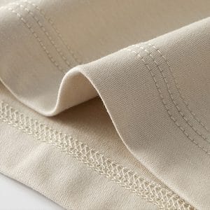 Close-up of beige fabric with visible double-stitched seams and folded edge.