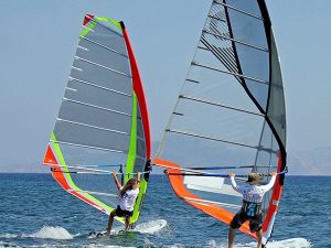 Two windsurfers glide across blue water, each holding a bright, colorful sail on a sunny day on the sea.