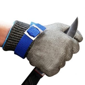 Close-up of a gloved hand gripping a knife blade, wearing a chainmail protective glove and a blue wrist strap for protection while cutting.