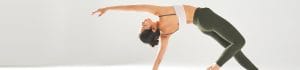 Woman performing a backbend yoga stretch in a bright studio, one arm extended forward and the other supporting her on the floor.