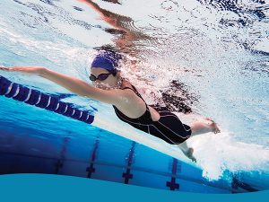 Swimmer in a black swimsuit and blue cap glides freestyle in a pool, wearing goggles beside a lane rope.