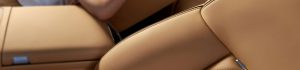 Close-up of tan leather car seat upholstery with visible stitching and a small silver latch in the lower left corner.