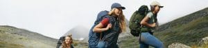 Three hikers with large backpacks trekking along a rocky mountain trail in misty terrain at dusk.