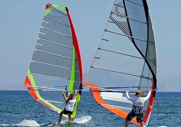 Two windsurfers glide across blue water, each holding a bright, colorful sail on a sunny day on the sea.