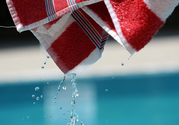 Red and white striped towel dripping water above a swimming pool surface
