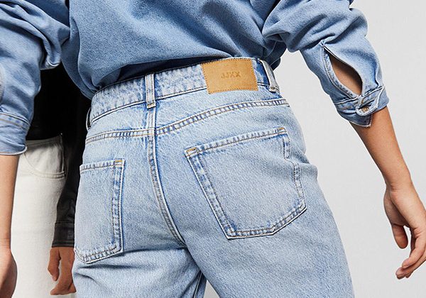 Back view of a person wearing light-wash jeans with a brown leather patch on the waistband and a blue denim shirt.