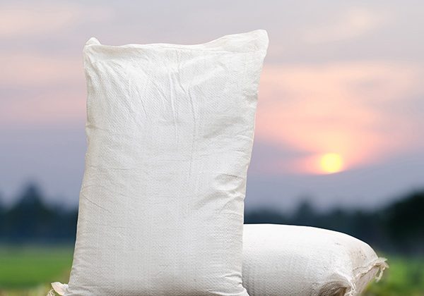 Two white sacks standing on bare soil with a sunset over a distant field behind them, suggesting an agricultural setting.