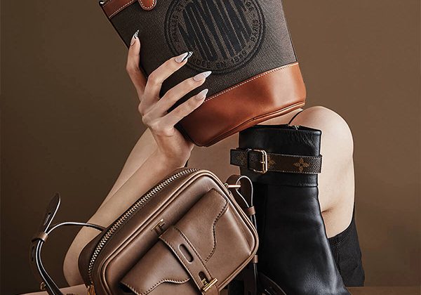 Close-up of fashion bags and a heeled boot arranged together: tan crossbody, brown leather pouch, and black ankle boot against a brown background.