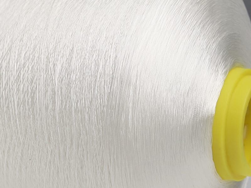 Close-up of white thread wound around a yellow spool core, showing detailed fibers in a textile setup.