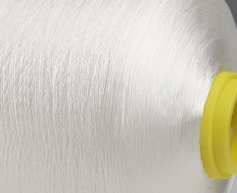 Close-up of white thread wound around a yellow spool core, showing detailed fibers in a textile setup.